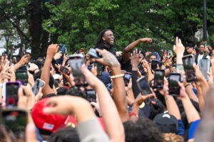 In Union Square, New York City, social media and streaming influencer Kai Cenat stands over a crowd of young people using their phones.